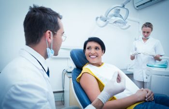 smiling woman sitting on dental chair and chat with doctor