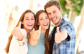 Two young women and a man with perfect smiles showing their thumbs up.