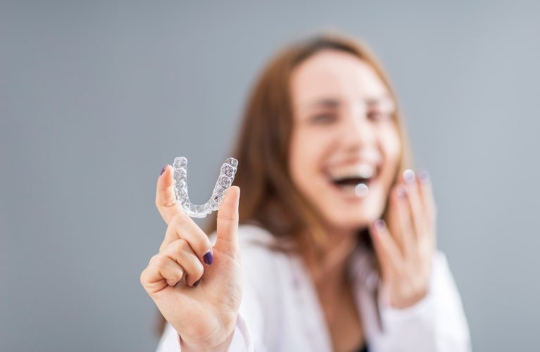 Beautiful smiling Turkish woman is holding an invisalign bracer in a studio with grey background