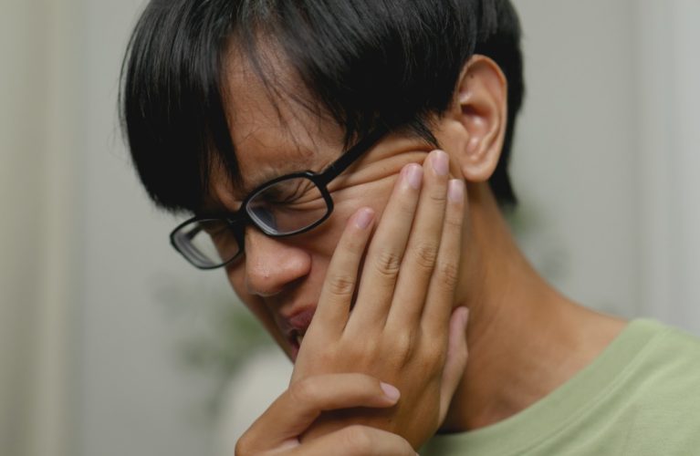 Asian man in severe toothache checking teeth with phone camera.